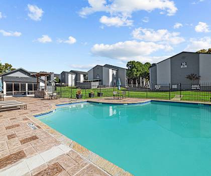 A swimming pool surrounded by a brick patio and a black fence.