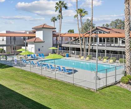 A pool surrounded by a fence with chairs and umbrellas.