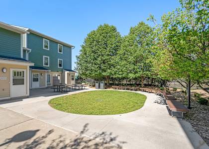 a circular lawn in front of two buildings with trees and a sidewalk