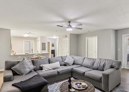 A grey sectional sofa with a black throw pillow sits in a living room with a ceiling fan and a coffee table.
