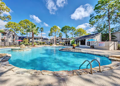 A swimming pool surrounded by trees and a building in the background.
