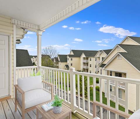 A white door is on the left of a balcony with a chair and a table.