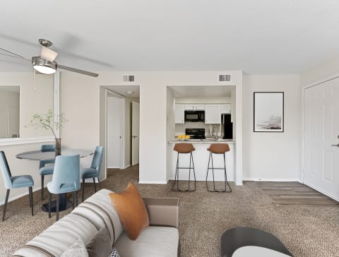 a living room with a couch and a chair in front of a kitchen with a breakfast bar at The Hudson, North Richland Hills, TX