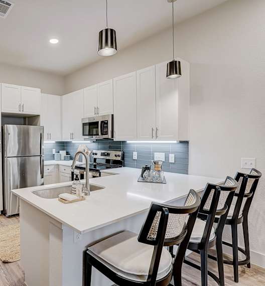 A kitchen with white cabinets and a white island with three chairs.