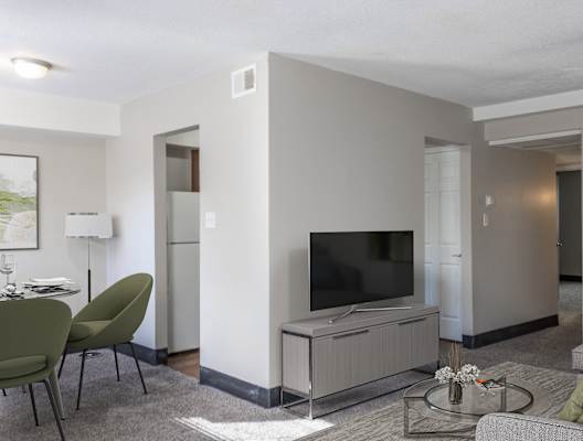 a living room with a television and a dining room in the background