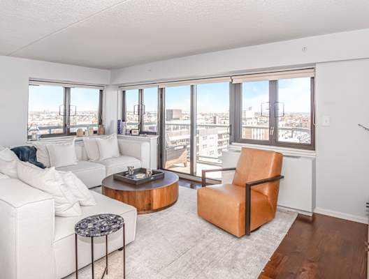 a living room with white couches and a table and a view of the city at 10 West Apartments, Long Beach, New York