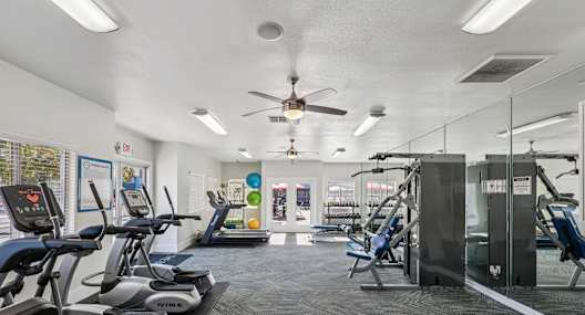 A gym with treadmills, exercise equipment, and a fan.