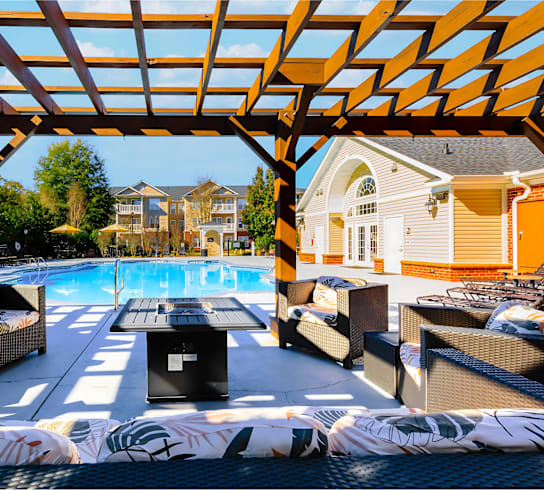 A pool area with a wooden pergola and lounge chairs.