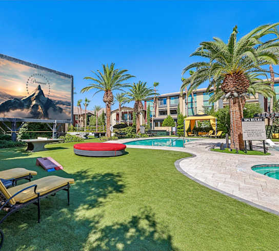 A sunny day at a resort with a pool, palm trees, and a mountain mural on the wall.