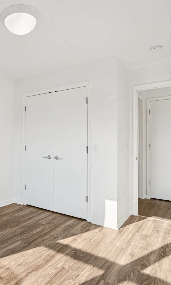 A room with white walls and wooden flooring with a door and two cabinets.