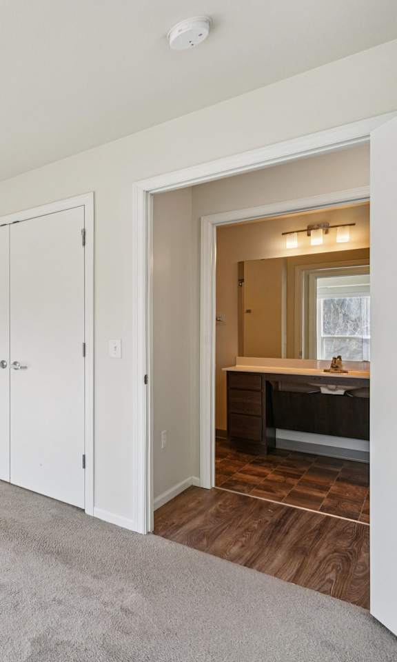 A room with white walls and a carpeted floor with a white door and a window.