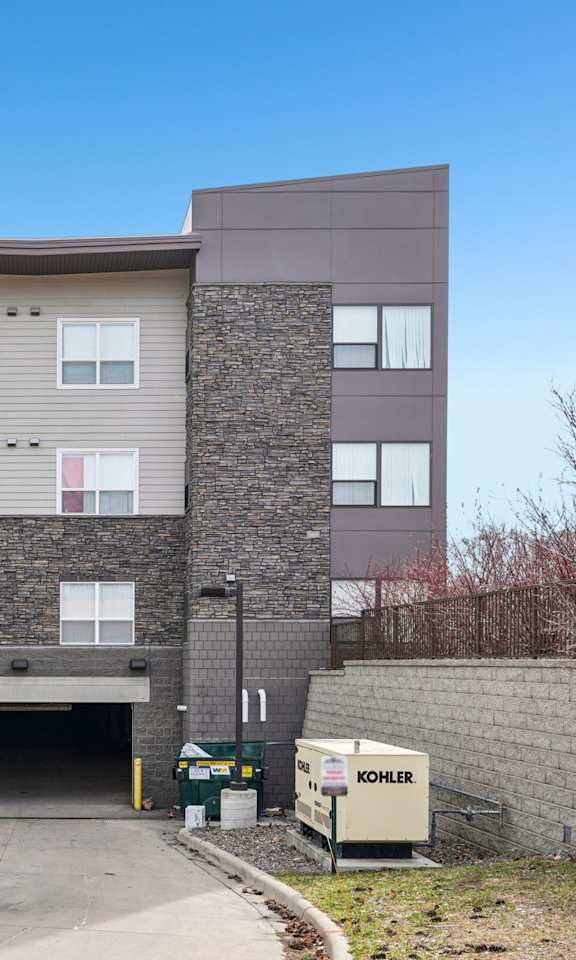 A modern building with a grey and brown facade and a stone wall in front.