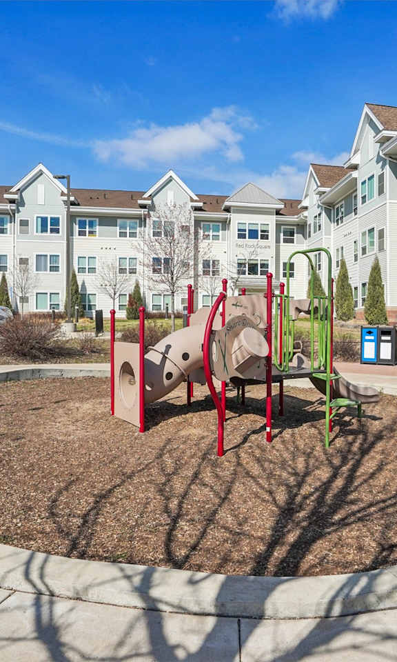 A playground with a red swing set in front of apartment buildings.