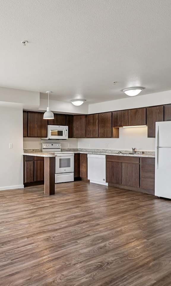 A spacious kitchen with wooden floors and white appliances.