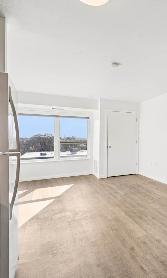 A white room with wood flooring and a window.