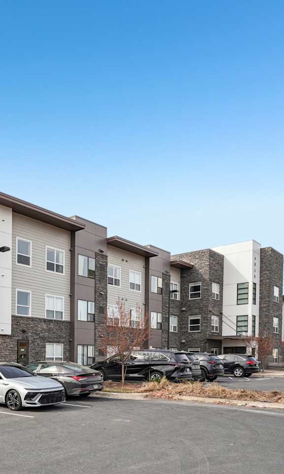 A parking lot in front of a multi-story apartment building with cars parked.