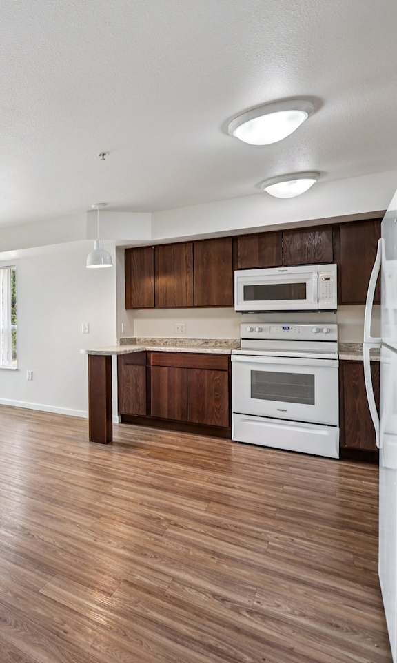 A kitchen with white appliances and wooden floors.
