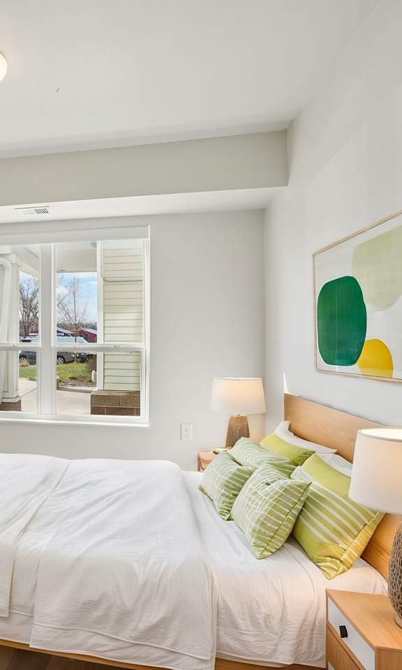 A bedroom with a large bed, a flat screen TV, and a window with blinds.