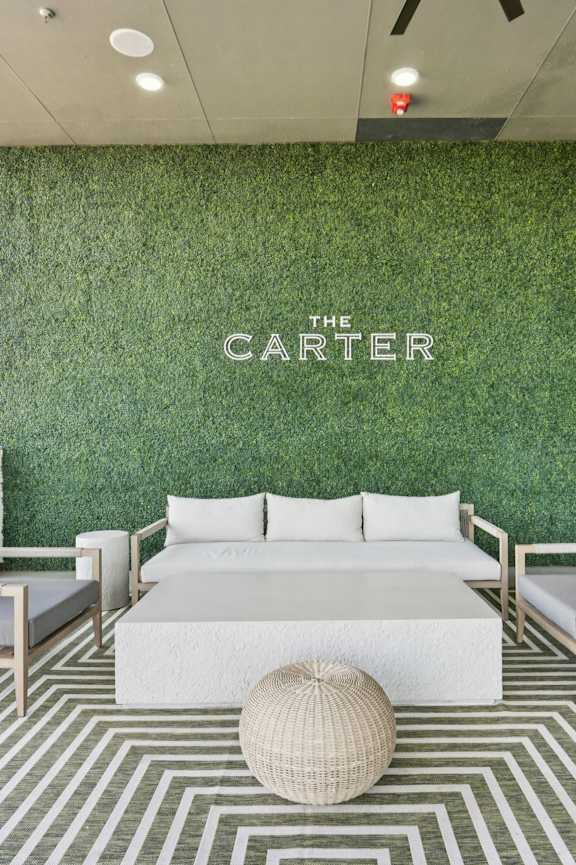 A white sofa and two chairs are arranged on a striped rug in front of a green wall with the word "CARTER" on it.