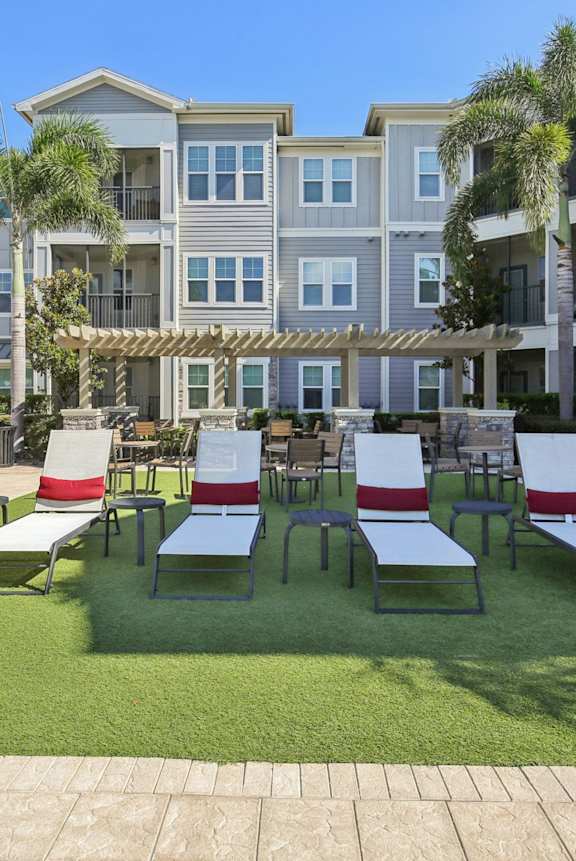 A sunny day at the apartment complex with a green lawn and white lounge chairs.
