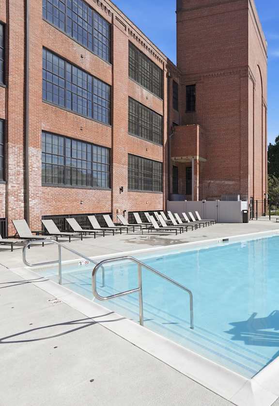 A swimming pool on a rooftop with lounge chairs and a building in the background.