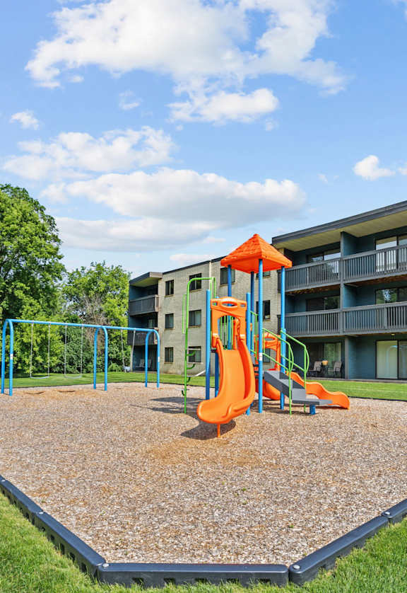 A playground with a slide and a swing set in front of apartment buildings.