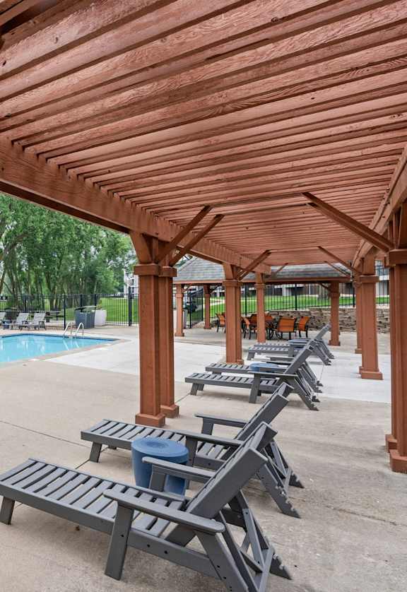 A wooden pergola overhangs a pool area with lounge chairs.