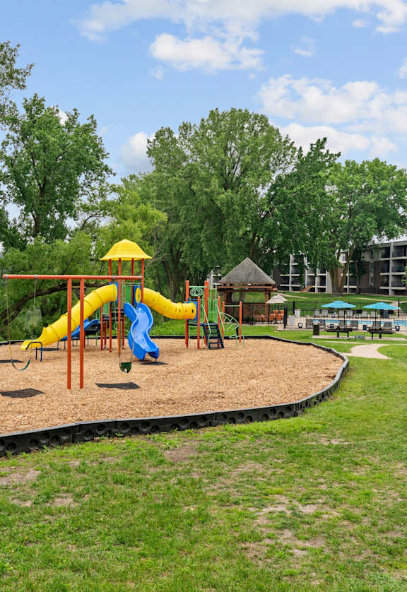 A playground with a yellow slide and a red swing set.