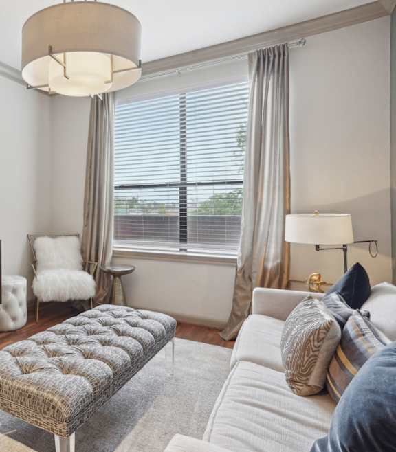 A living room with a grey sofa, a grey rug, a grey coffee table, a grey side table, a grey armchair, a grey chair, a grey lamp, a grey wall, a grey floor, a grey ceiling,