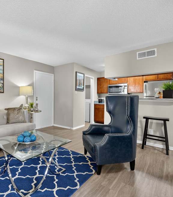 A living room with a grey sofa, a glass coffee table, and a blue patterned rug.
