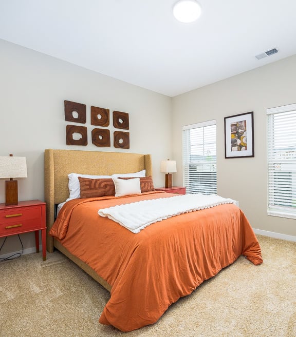 a bedroom with an orange bed and two windows