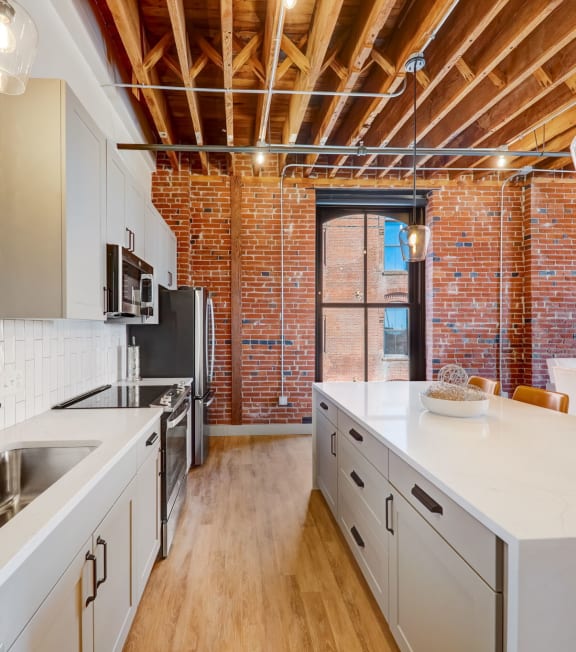 a kitchen with a large white counter top and a exposed brick wall at Greeley Lofts, St. Louis, MO, 63102