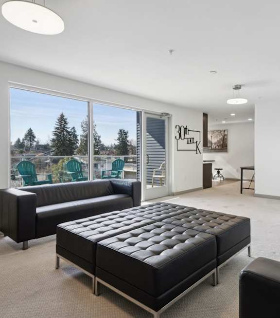 A black leather couch sits in a bright room with a large window.