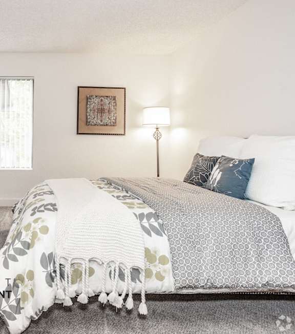 A well-lit bedroom with a large bed and a painting on the wall.