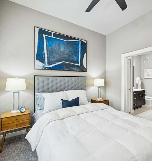 A bedroom with a large bed, a ceiling fan, and a painting on the wall.