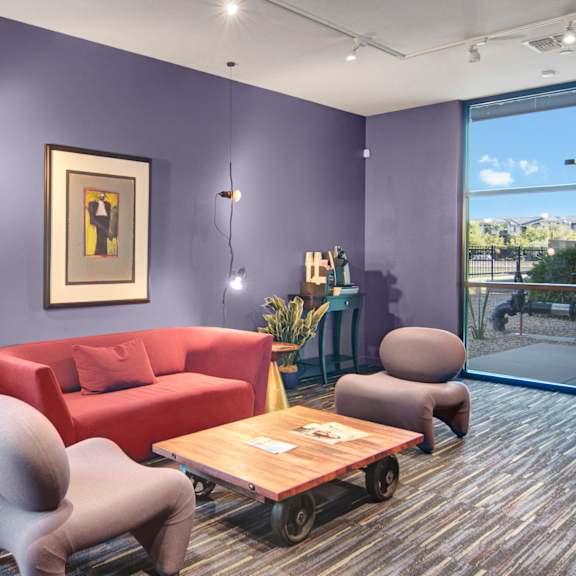 A living room with a red couch, plush purple chairs, and coffee tables at the Trend at 51 Apartment Homes. 
