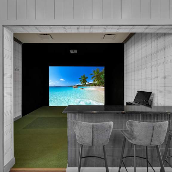 A room with a bar and chairs with a screen on the wall.