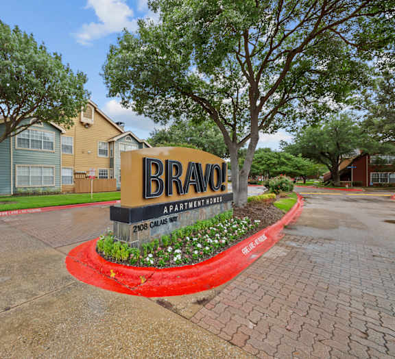 A sign for Bravo Apartments is in front of some trees and buildings.