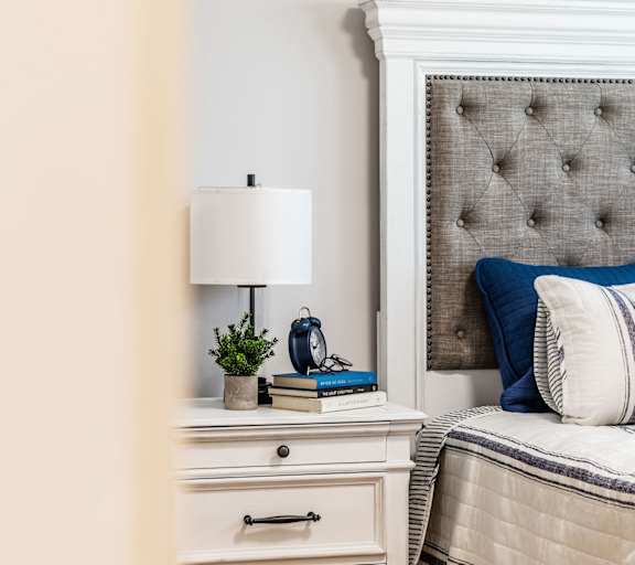A bedroom with a bed, a nightstand with a lamp, and a plant.