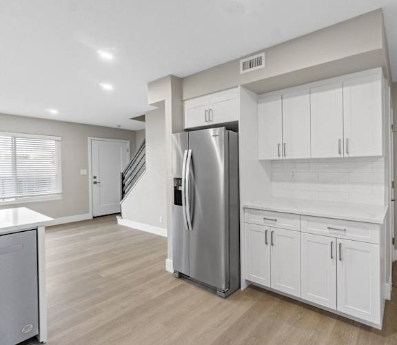 A kitchen with a refrigerator, cabinets, and a staircase.