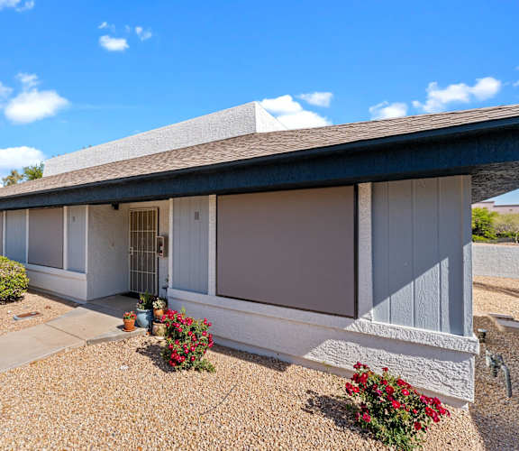 A house with a grey roof and white walls with a gravel driveway in front.