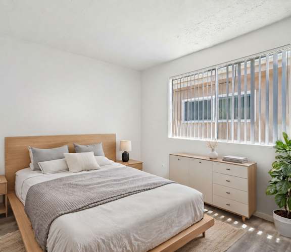 A bedroom with a large bed, a nightstand with a lamp, and a plant.