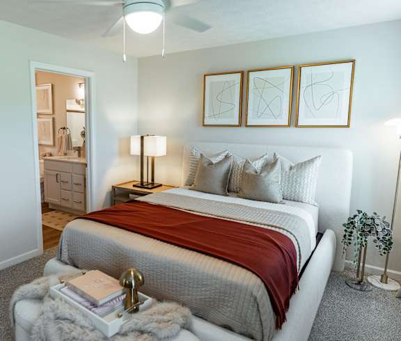 A bedroom with a bed, nightstand, and a plant.