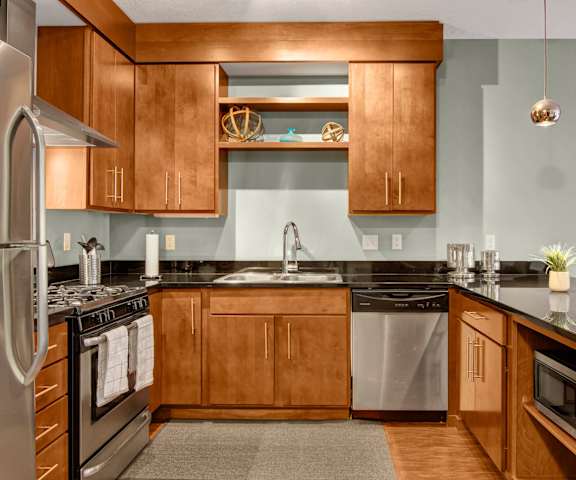 A large kitchen with stainless steel appliances, black countertops, and large, luminous wooden cabinets at Vue Apartment Homes. 