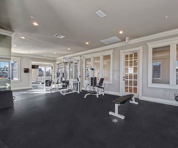 A gym with cardio machines, windows, TVs, and weights at Memorial Creek Apartments. 