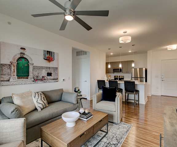 The living room with a couch, coffee table, decorations, a TV, and a view of the kitchen with gray cabinets and stainless-steel appliances at Florence at the Harbor.