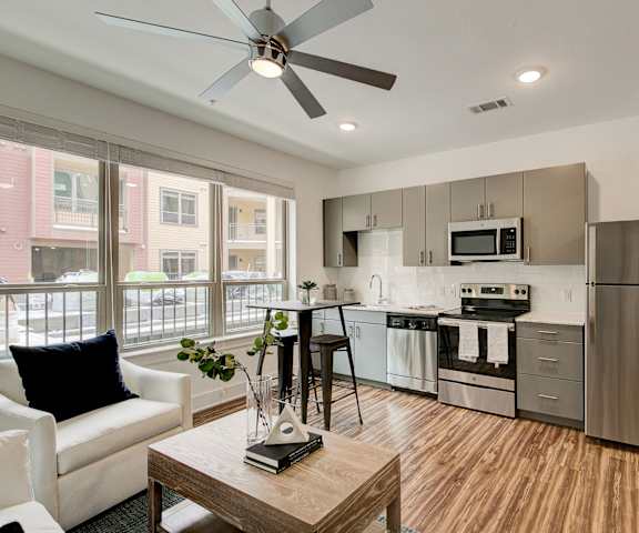 The living room with a couch, chairs, and a coffee table leading into a kitchen with grey cabinets and stainless-steel appliances at Florence at the Harbor. 