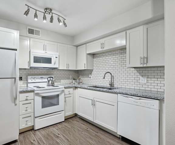A white kitchen with a refrigerator, microwave, oven, and sink.
