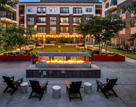 an outdoor patio with chairs and a fire pit in front of an apartment building