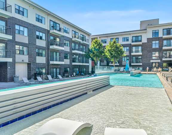a swimming pool with lounge chairs and umbrellas in front of an apartment building